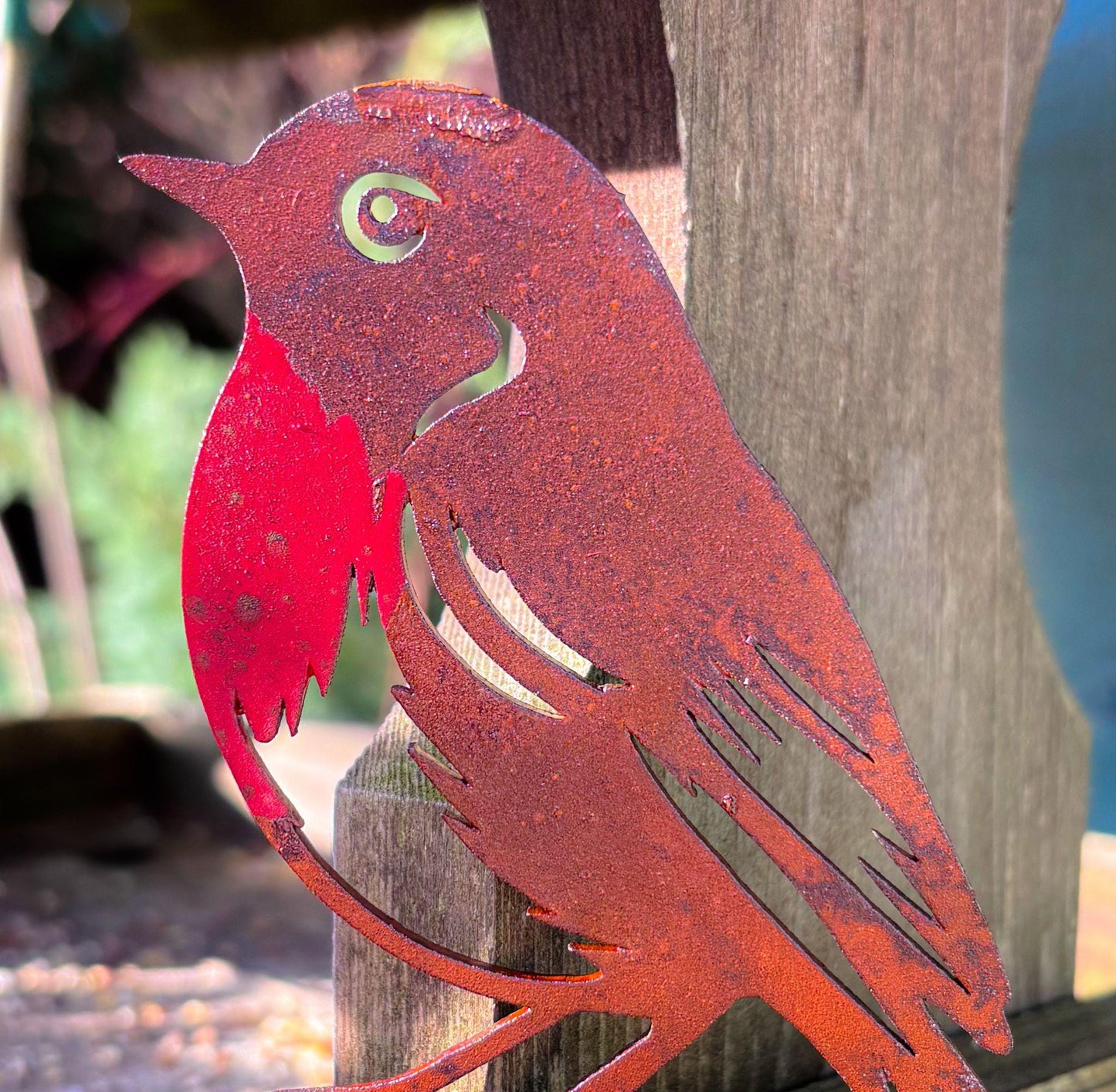 Metal bird sculpture with a red breast on a wooden post