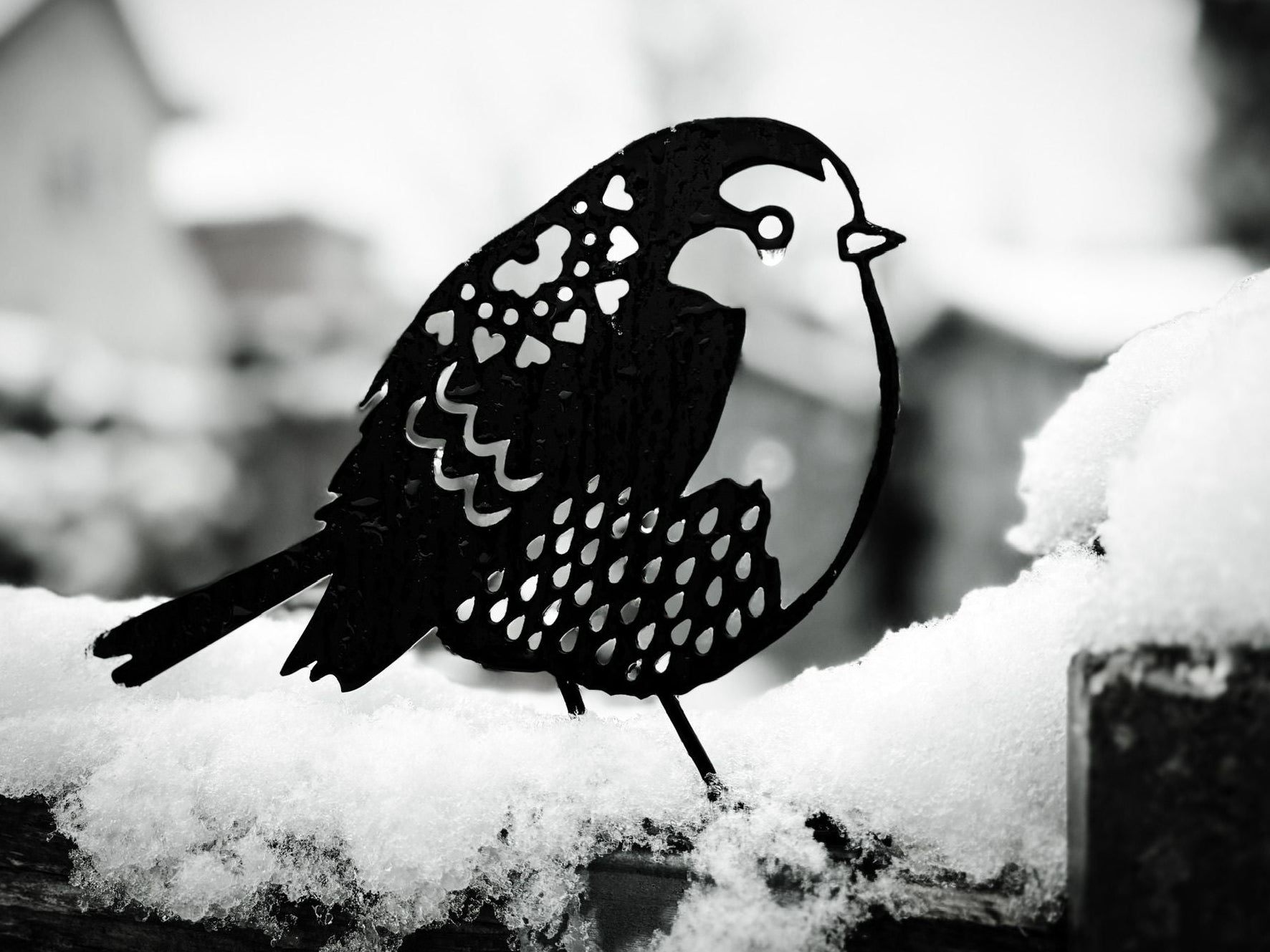 Metal bird ornament on a snowy surface with a blurred background